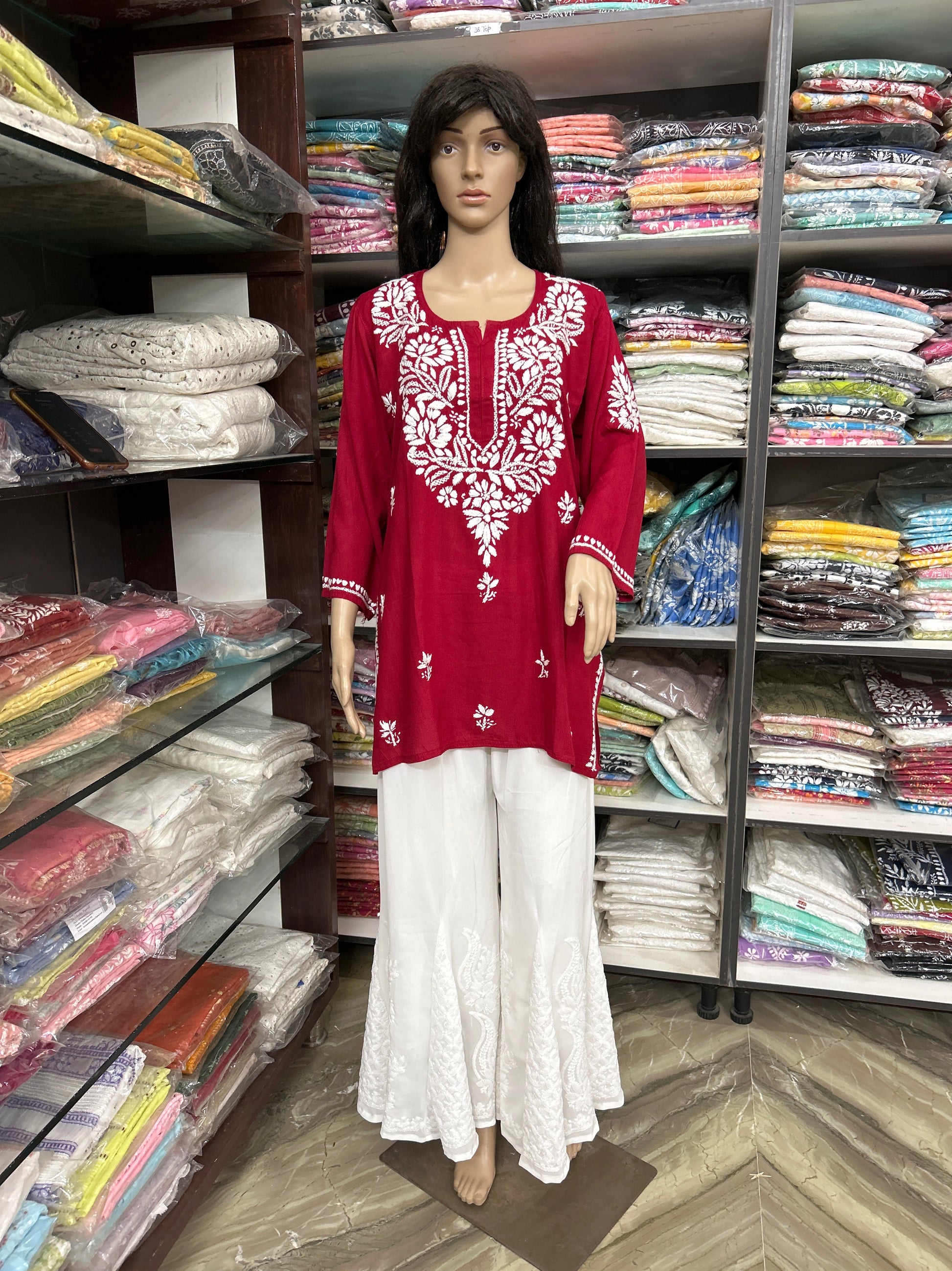Mannequin wearing a red embroidered top and white pants in a fabric store.