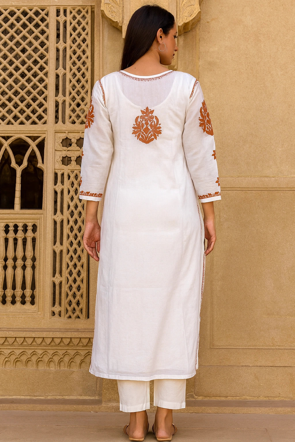 Woman wearing a white kurta with orange embroidery in front of a beige wall.