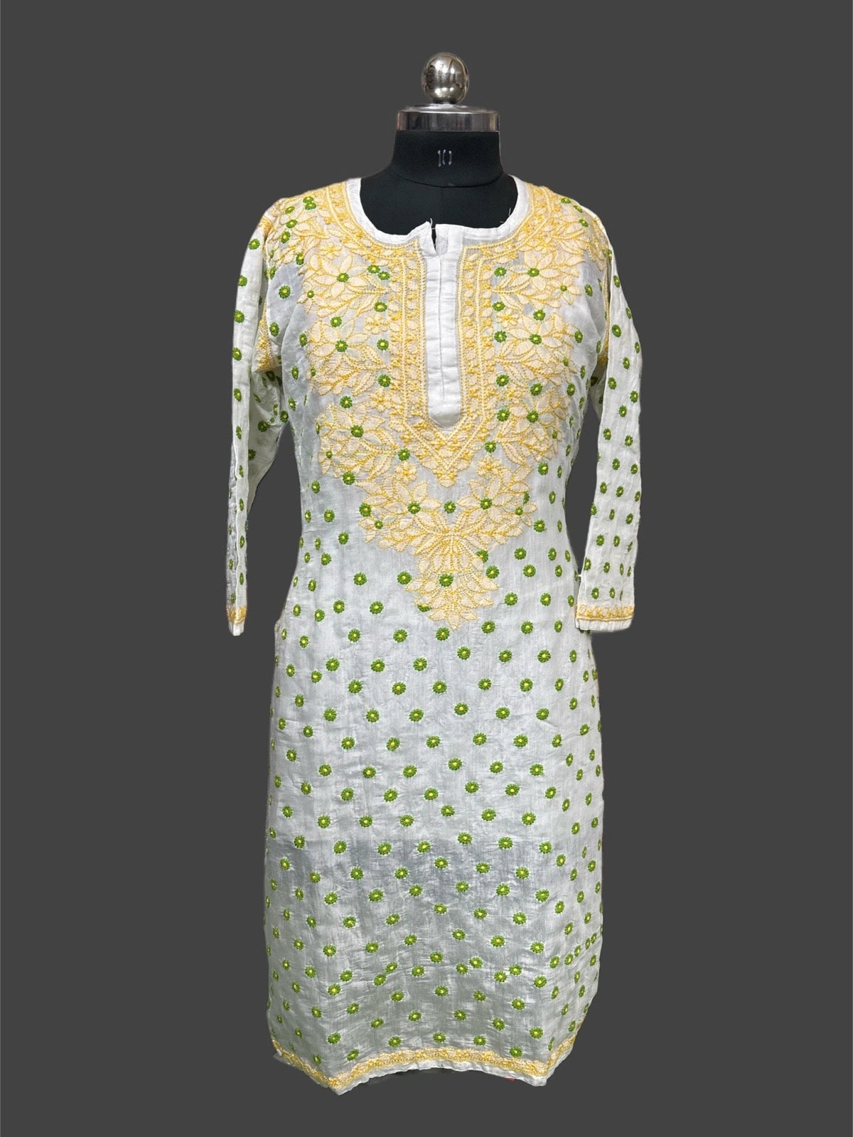 White dress with green floral patterns and yellow embroidery on a mannequin against a gray background