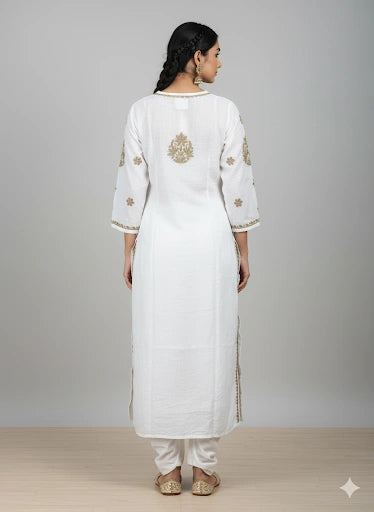 Woman wearing a white kurta with gold embroidery on a plain background