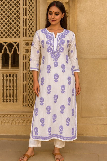 Woman wearing a lucknowi chikankari  white kurta with purple floral patterns in front of a decorative wall.