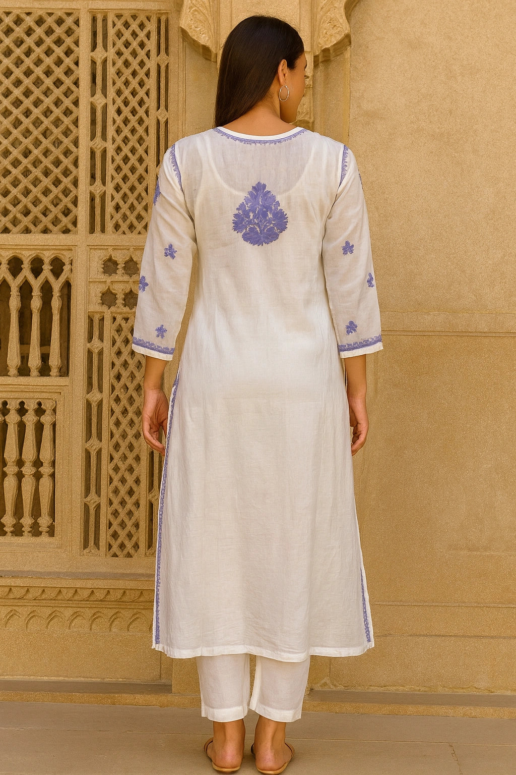 Woman wearing a lucknowi chikankari  white kurta with blue embroidery in front of a beige wall.