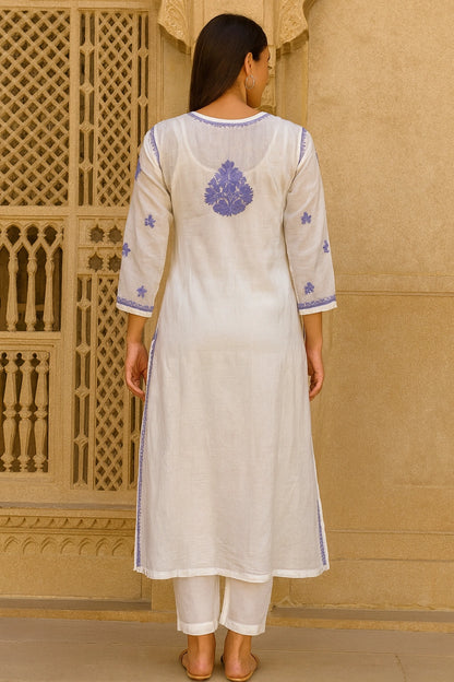 Woman wearing a lucknowi chikankari  white kurta with blue embroidery in front of a beige wall.