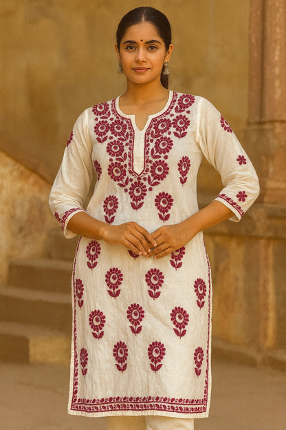 Woman wearing a lucknowi chikankari  white kurta with red floral patterns against a beige wall.