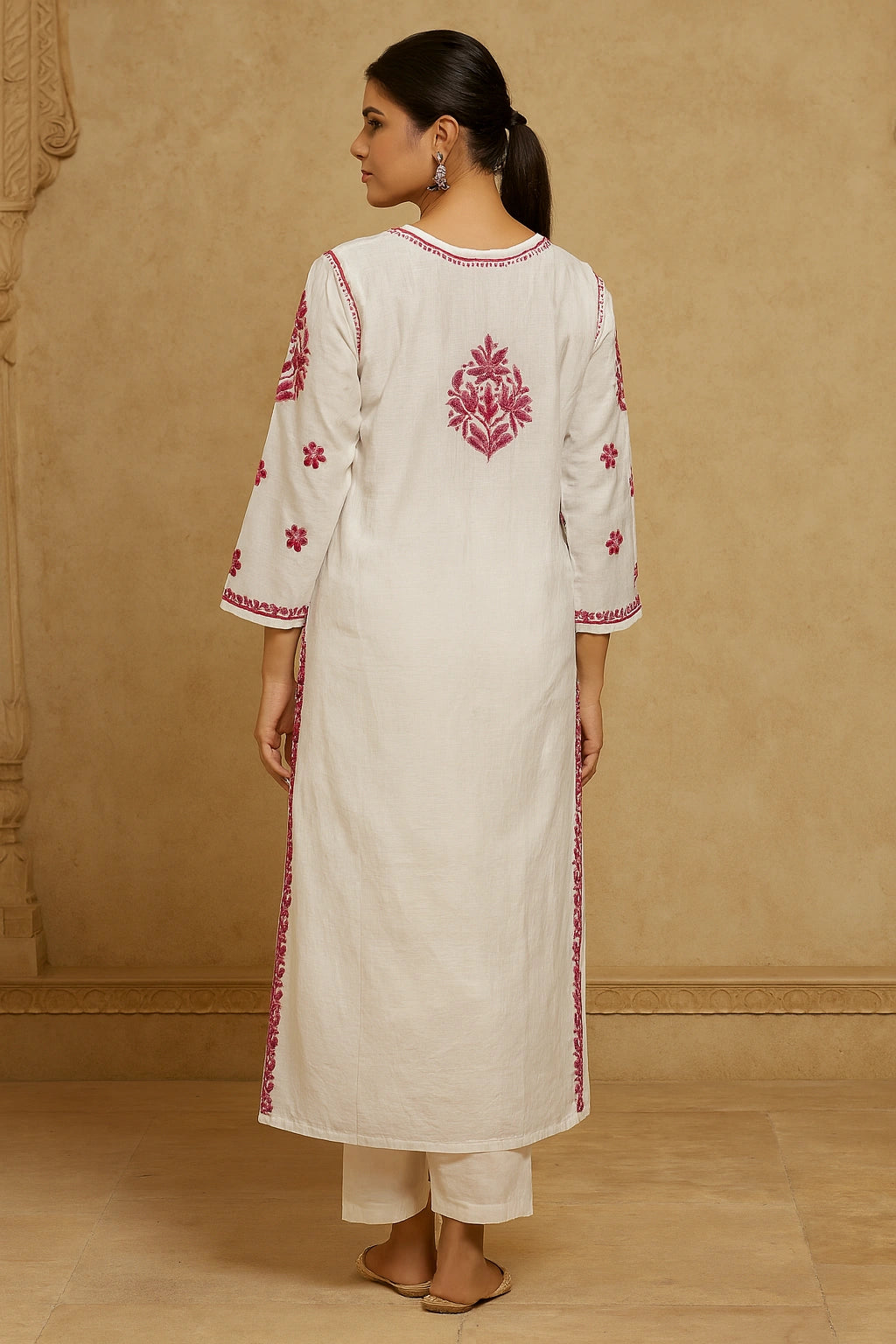 Woman wearing a white kurta with red embroidery against a beige wall.