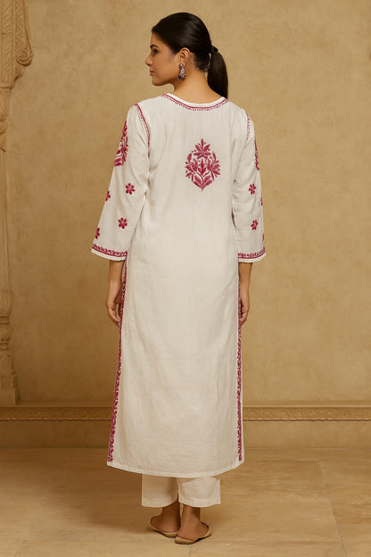 Woman wearing a white kurta with red embroidery against a beige wall.