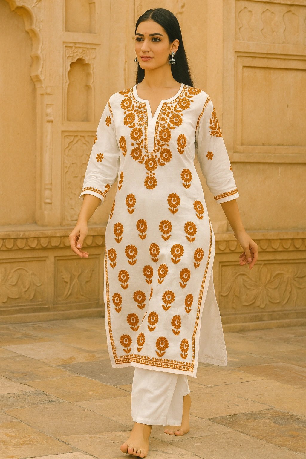 lucknowi chikankari Woman wearing a white traditional outfit with orange floral patterns against a beige wall.