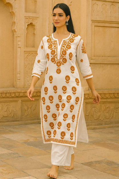lucknowi chikankari Woman wearing a white traditional outfit with orange floral patterns against a beige wall.