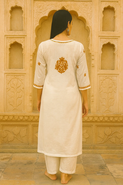 Person wearing a lucknow chikankari  cream kurta with gold embroidery in front of an ornate beige wall.
