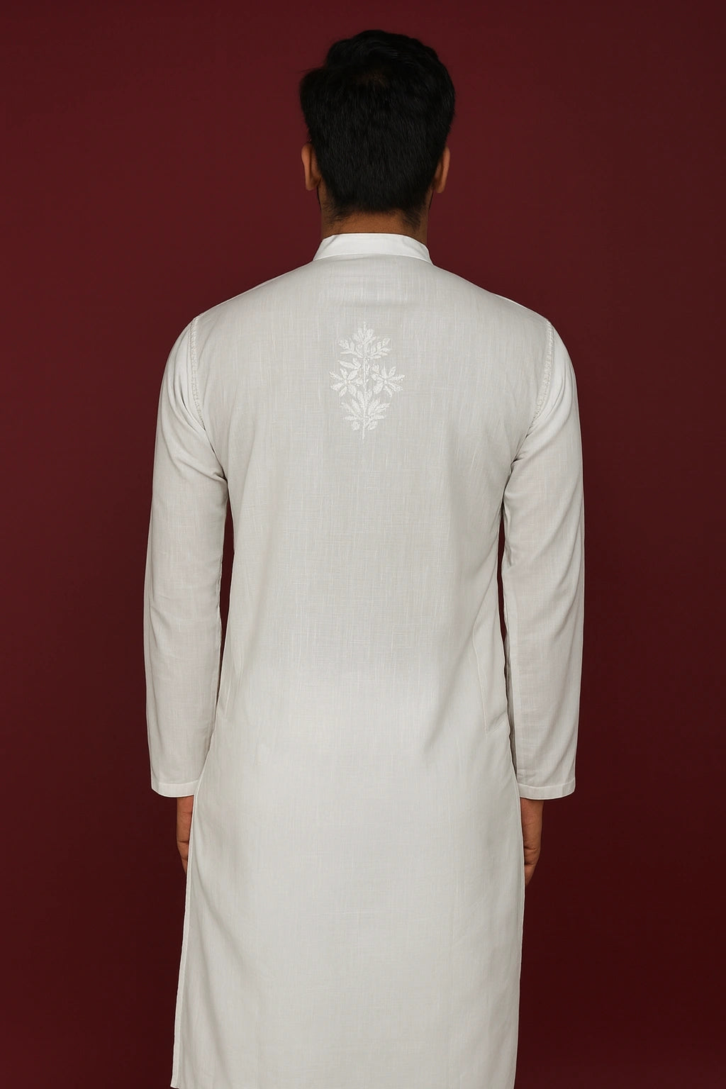 Man wearing a lucknowi chikankari light-colored kurta with an embroidered design on the back against a dark red background