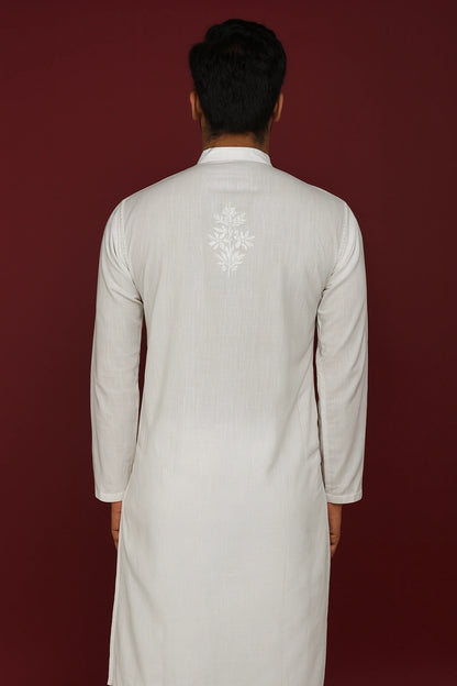 Man wearing a lucknowi chikankari light-colored kurta with an embroidered design on the back against a dark red background
