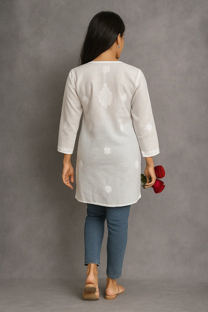 Woman wearing a lucknowi chikankari light gray floral patterned kurta with blue jeans against a gray background