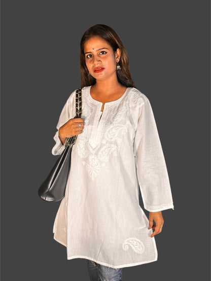 Woman wearing a white embroidered top holding a black handbag on a gray background