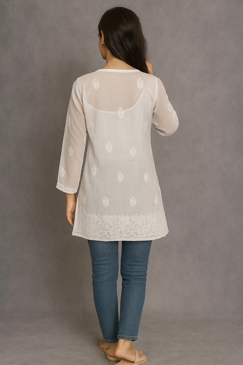 Woman wearing a lucknowi chikankari light-colored top with floral patterns and blue jeans on a gray background