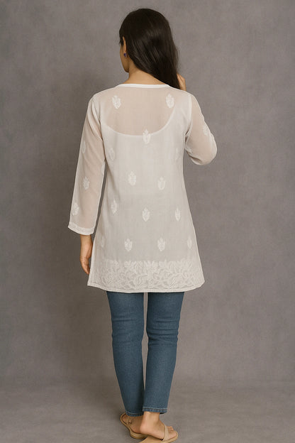 Woman wearing a lucknowi chikankari light-colored top with floral patterns and blue jeans on a gray background
