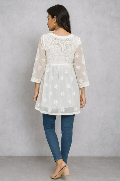 Woman wearing a lucknowi chikankari white lace top with sheer sleeves and blue jeans against a gray background