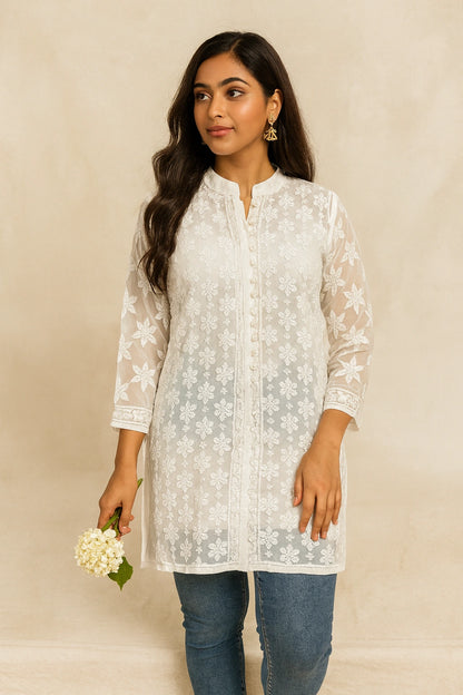 Woman wearing a lucknowi chikankari white floral lace top with blue jeans against a beige background
