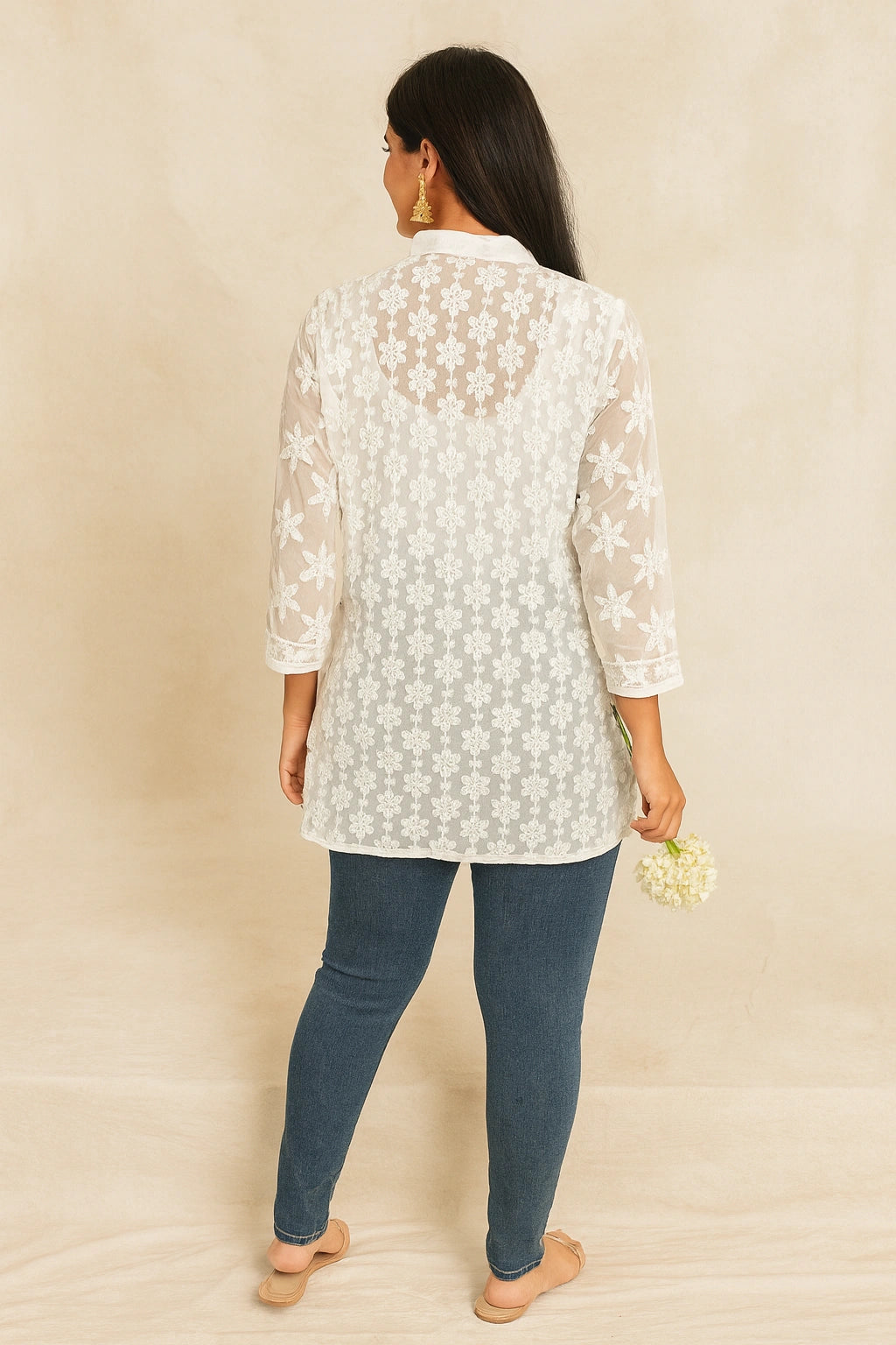 Woman wearing a lucknowi chikankari  light-colored floral lace top and dark blue jeans against a beige background