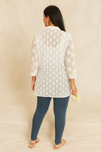Woman wearing a lucknowi chikankari  light-colored floral lace top and dark blue jeans against a beige background