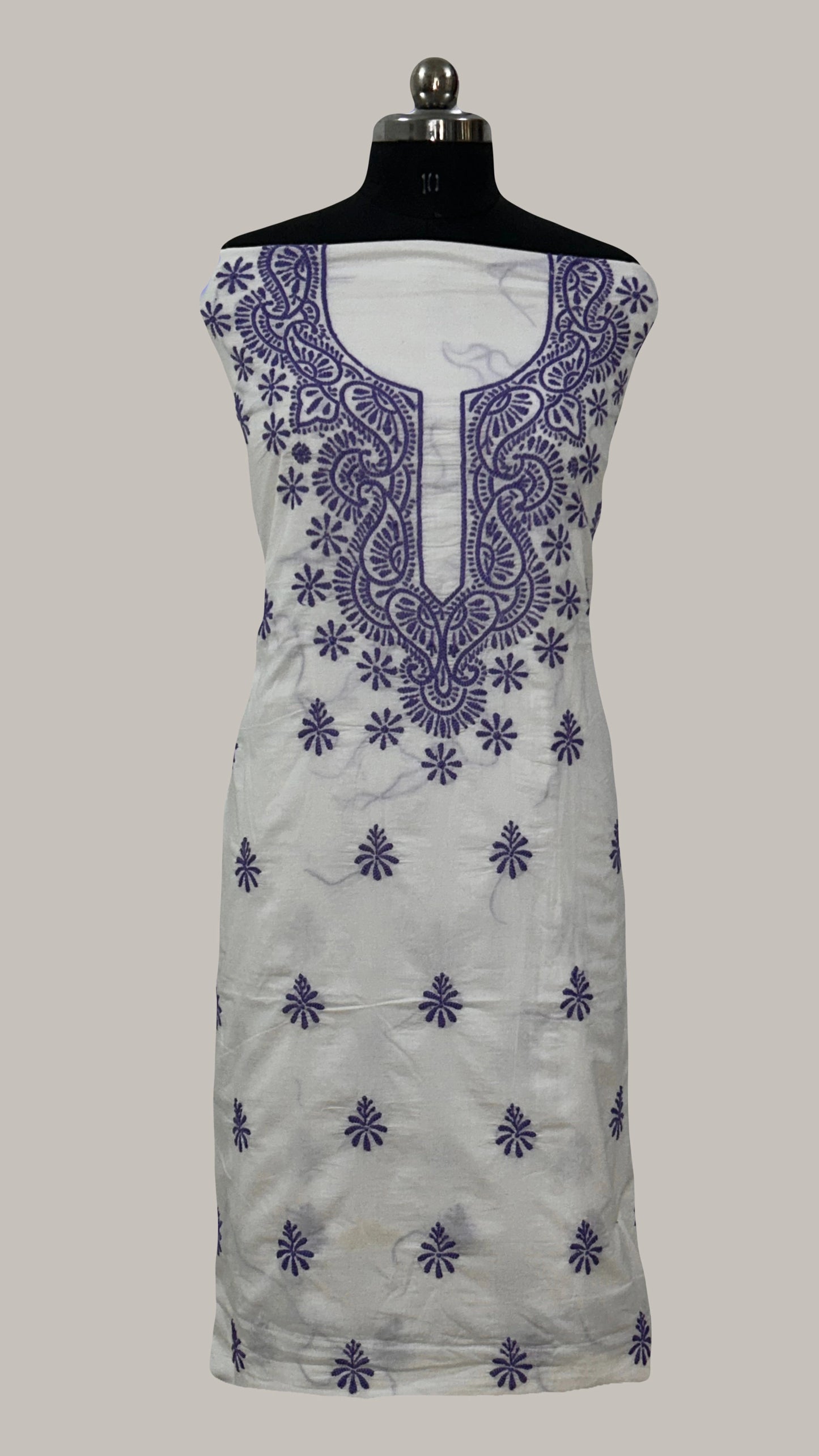 White dress with purple floral embroidery on a mannequin against a gray background