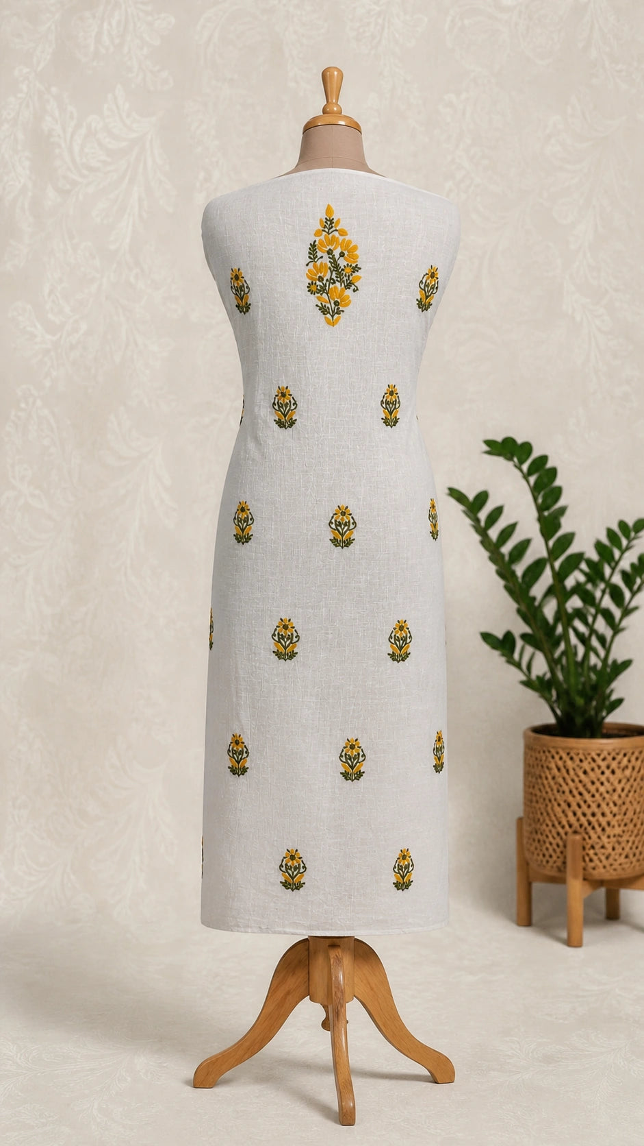 White dress with gold embroidery on a mannequin against a neutral background