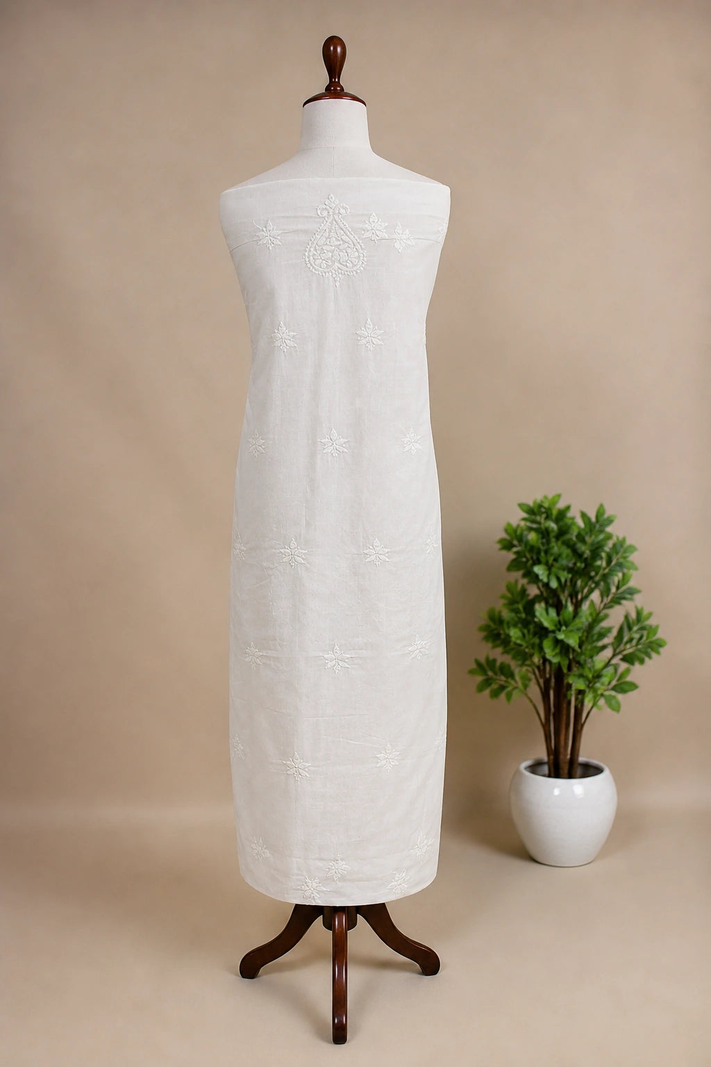 Lucknowi chikankari white dress with floral patterns on a mannequin against a gray wall with decorative panels.
