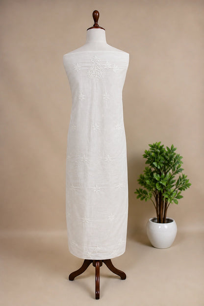 Lucknowi chikankari white dress with floral patterns on a mannequin against a gray wall with decorative panels.