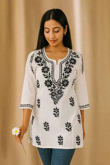 Woman wearing a white top with black floral embroidery against a beige background