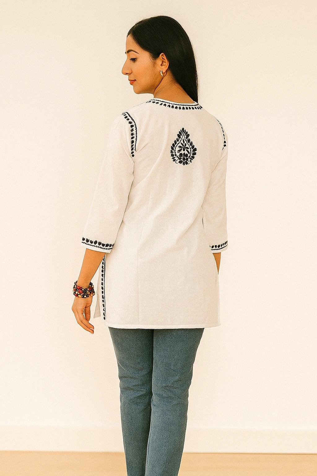 Woman wearing a white embroidered top with blue pants on a beige background