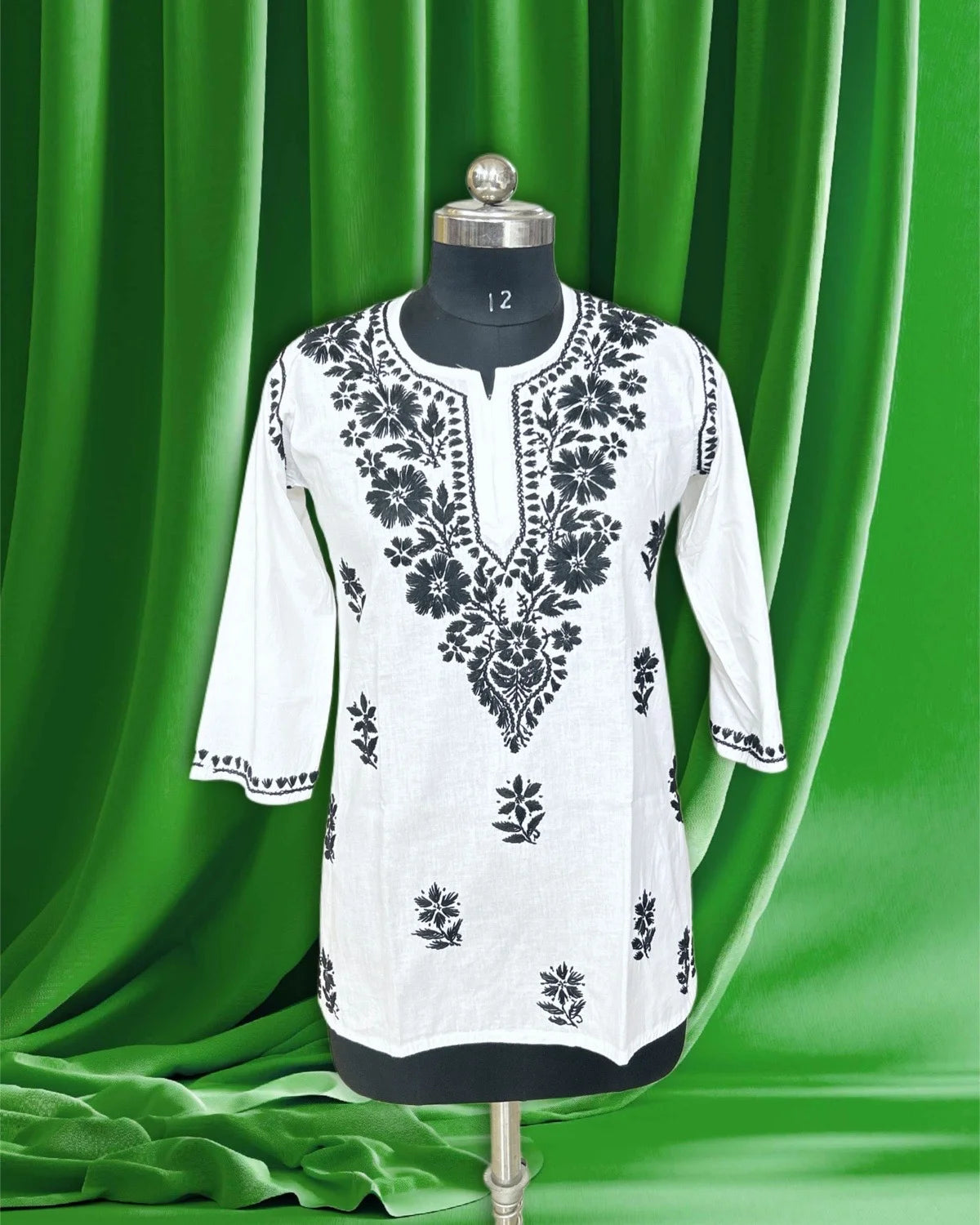 White kurta with black embroidery on a mannequin against a green curtain background