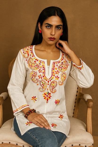 Woman wearing a white embroidered top sitting on a beige chair against a brown background
