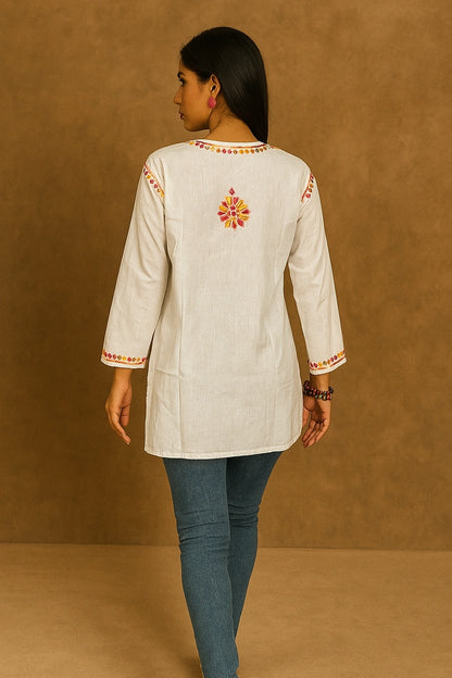 Woman wearing a cream-colored embroidered top with blue pants against a brown background