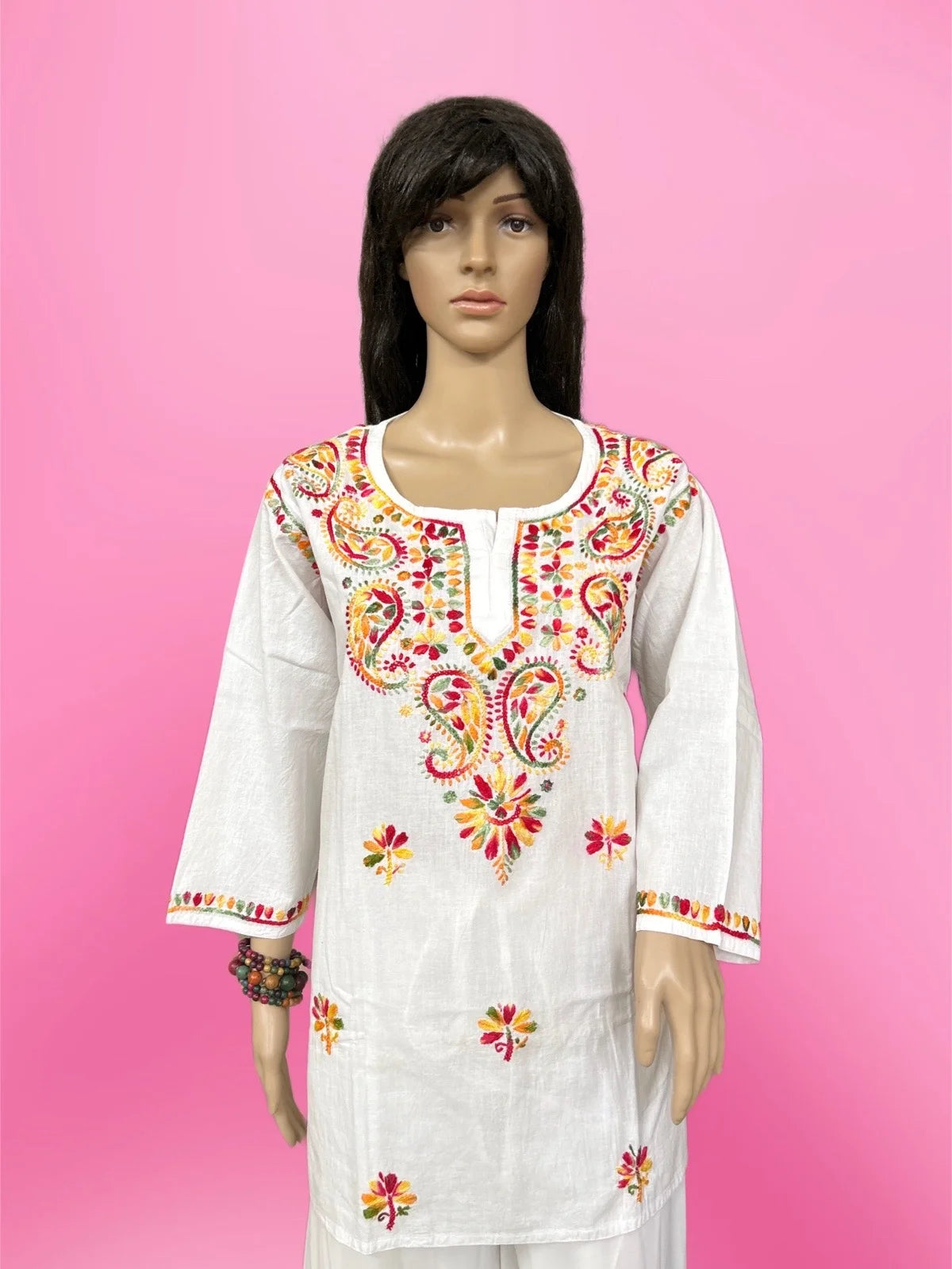 White embroidered dress with colorful patterns on a pink background