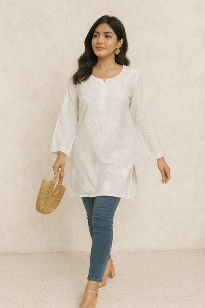 lucknowi chikankari Woman wearing a white long-sleeve top and blue jeans, holding a woven handbag against a plain background