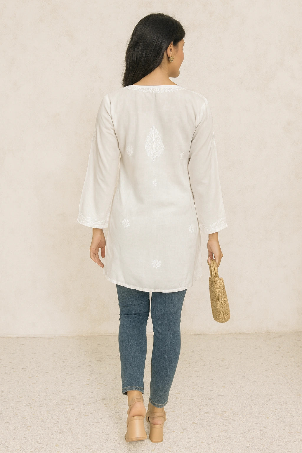 lucknowi chikankari Woman wearing a white long-sleeve top and blue jeans, holding a woven bag on a beige background