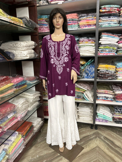 Mannequin wearing a purple embroidered top and white pants in a fabric store.