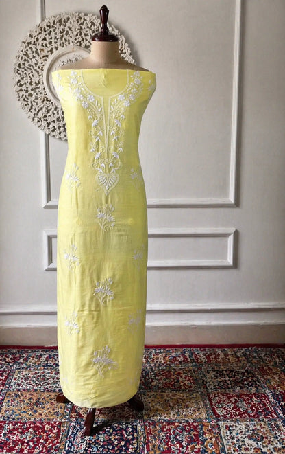Yellow dress with white embroidery on a mannequin against a decorative wall.