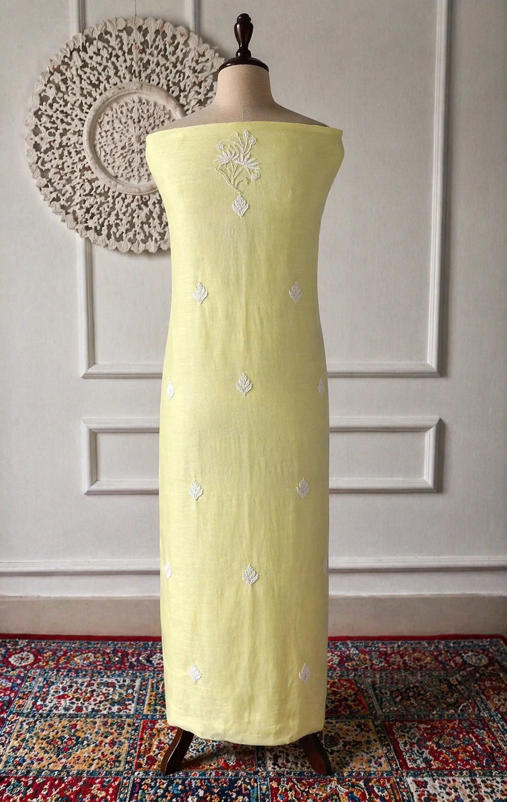 Light green dress with silver embroidery on a mannequin against a decorative wall.