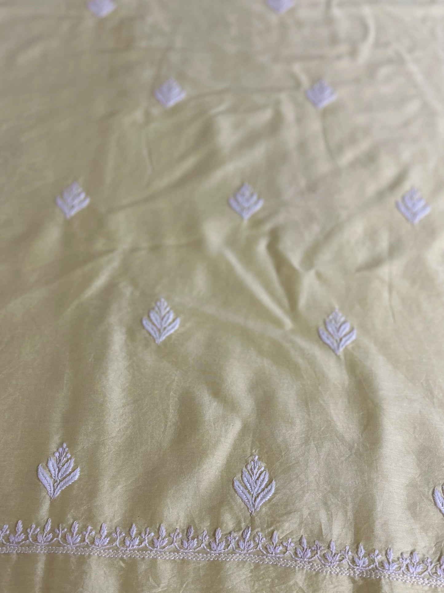Light green fabric with white floral embroidery on a beige background