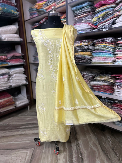 Yellow embroidered dress on a mannequin with a background of fabric shelves.