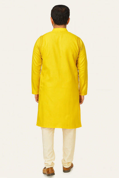 Man wearing a lucknowi chikankari  yellow kurta with white pants on a light gray background