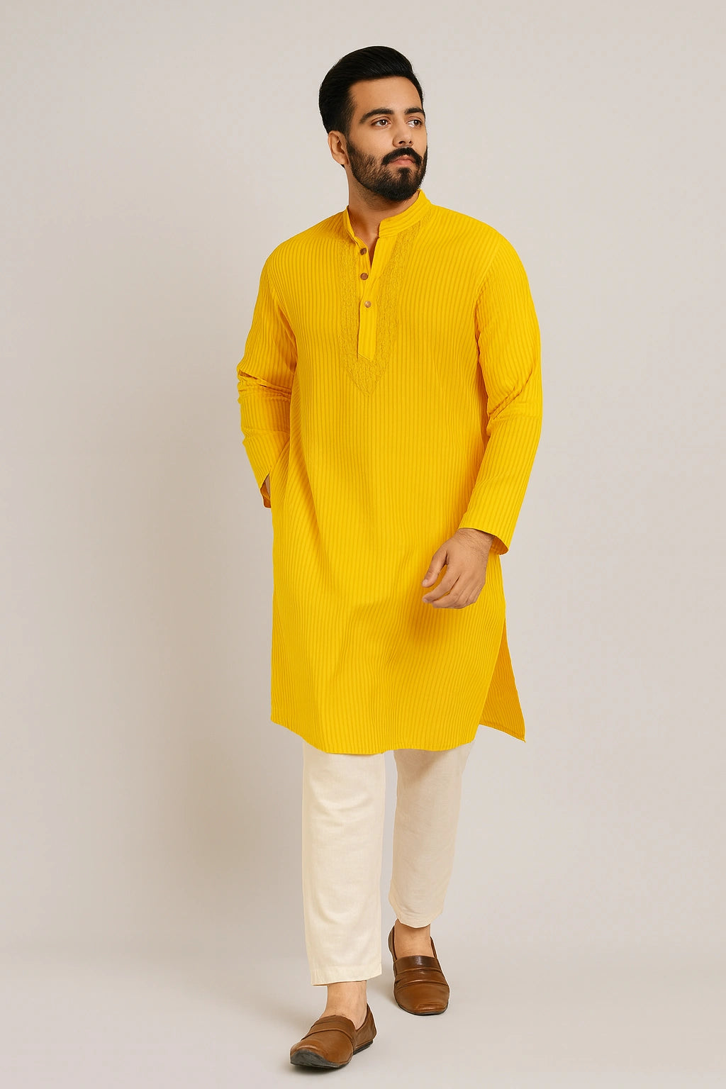 Man wearing a lucknowi chikankari yellow kurta with white pants on a plain background