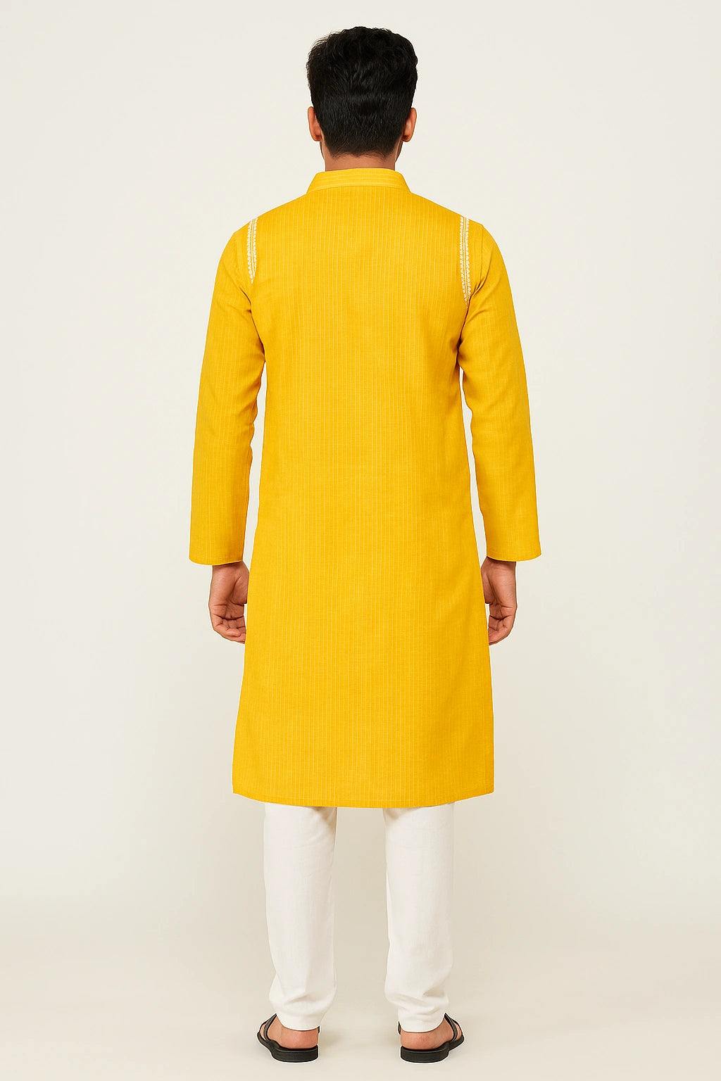 Person wearing a lucknowi chikankari yellow kurta with white pants on a light beige background