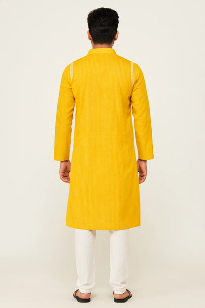 Person wearing a lucknowi chikankari yellow kurta with white pants on a light beige background
