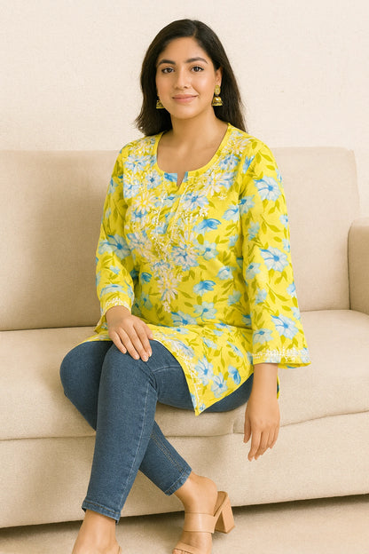 Woman wearing a lucknowi chikankari yellow floral top sitting on a beige couch.