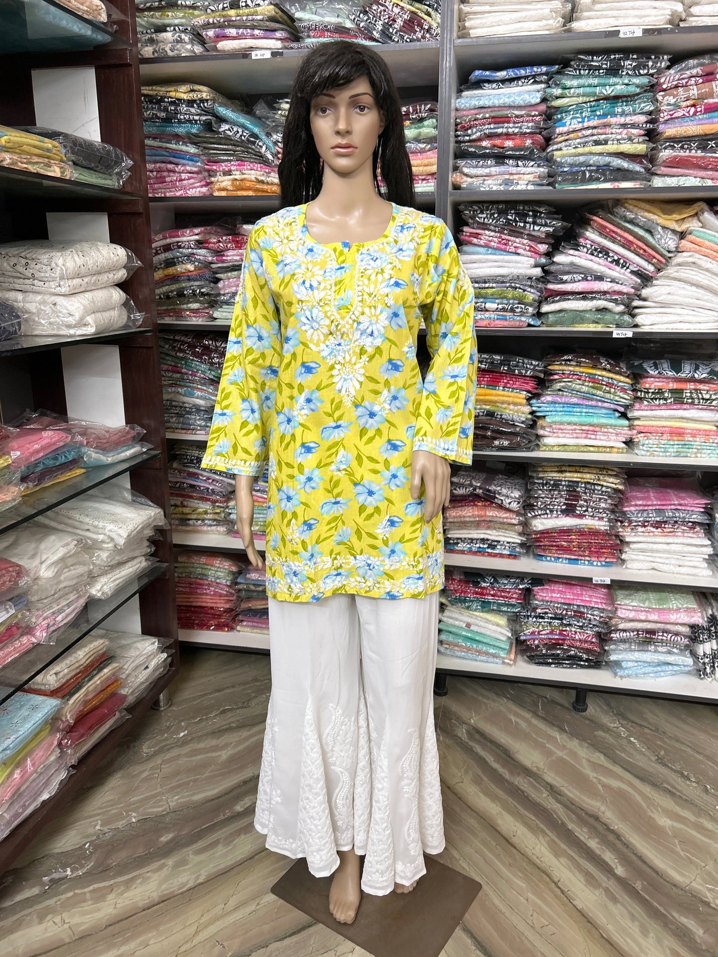 Mannequin wearing a lucknowi chikankari yellow floral top and white pants in a fabric store.