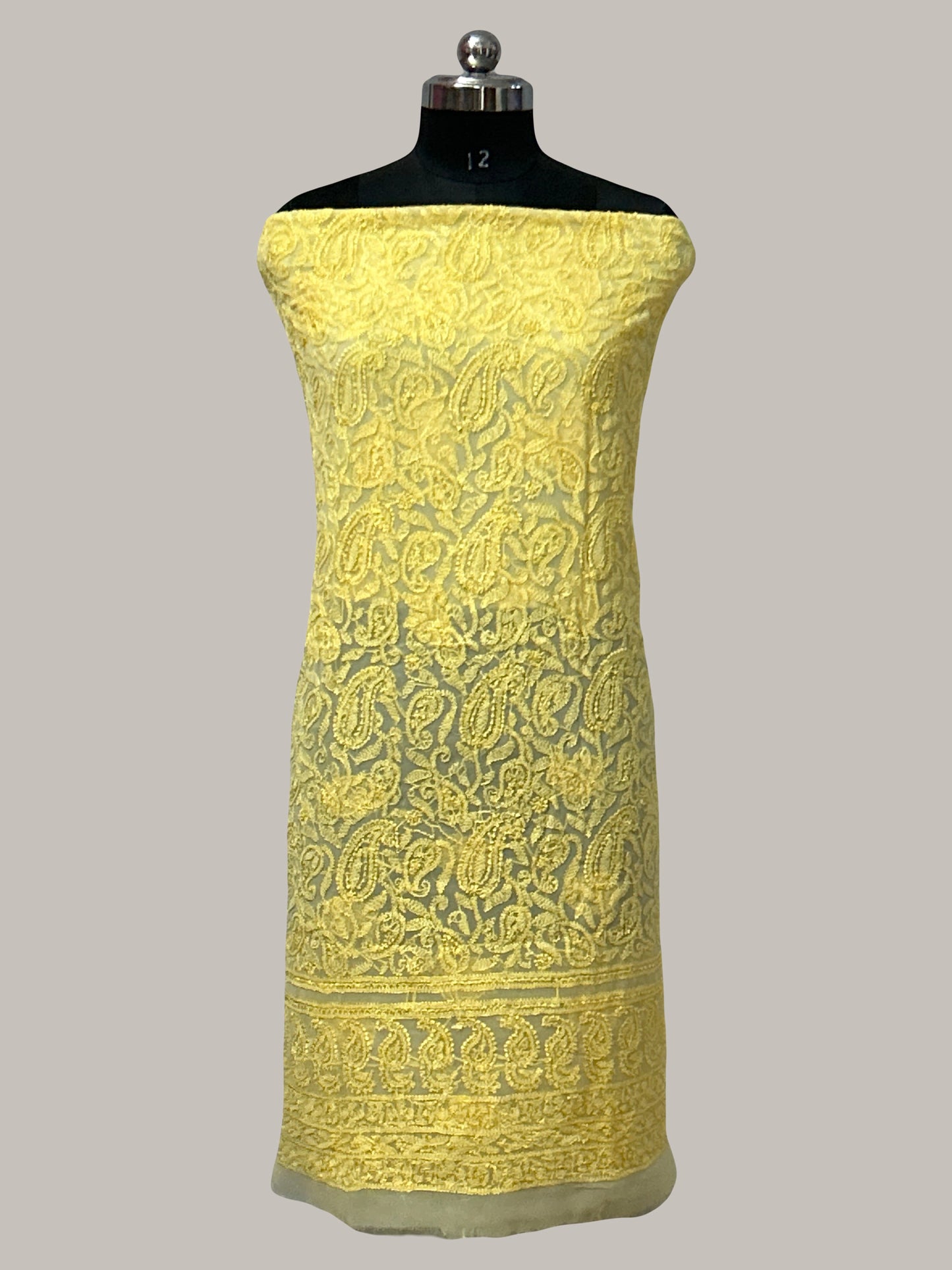 Yellow embroidered fabric on a mannequin against a gray background