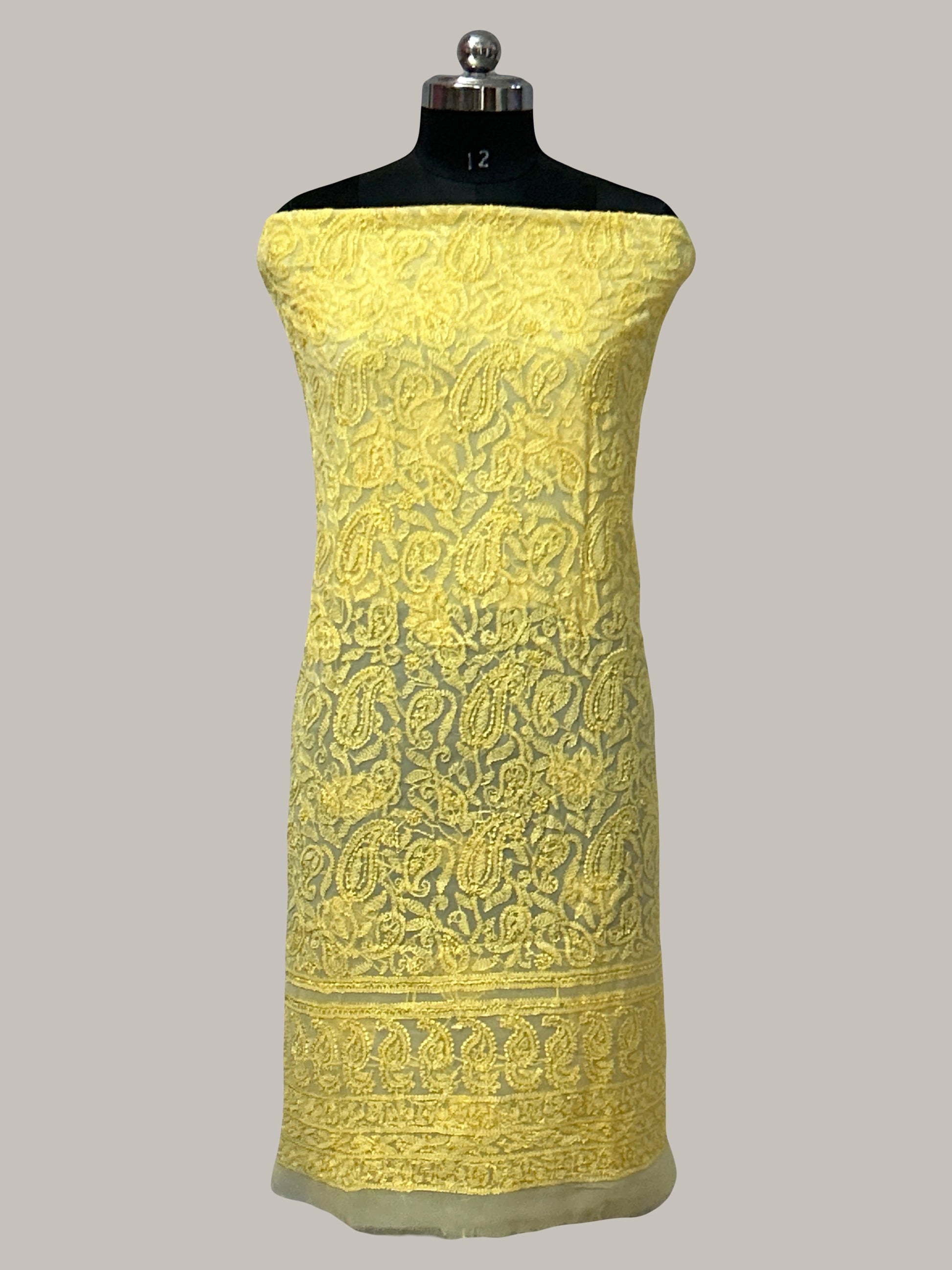 Yellow embroidered fabric on a mannequin against a gray background