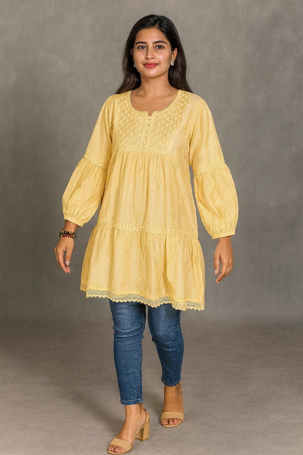 Woman wearing a lucknowi chikankari yellow dress with blue jeans against a gray background