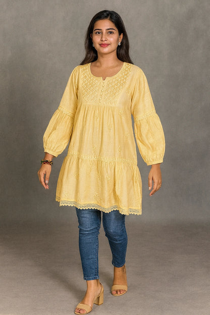Woman wearing a lucknowi chikankari yellow dress with blue jeans against a gray background